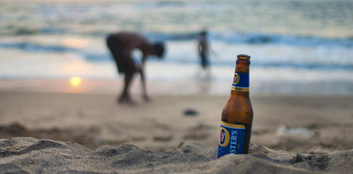 Una botella de cerveza en la playa y unos niños al fondo