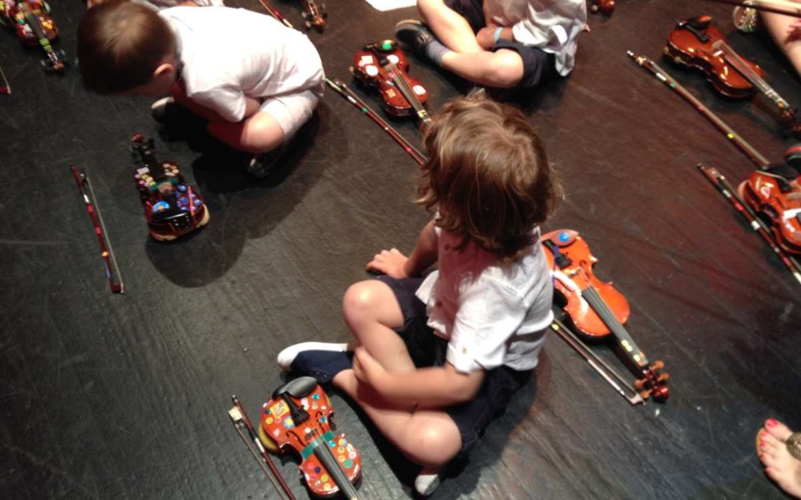 Niñoss sentados en el suelo con violines