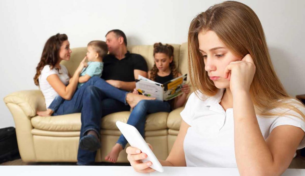 Una adolescente consulta el móvil y su familia juega al fondo