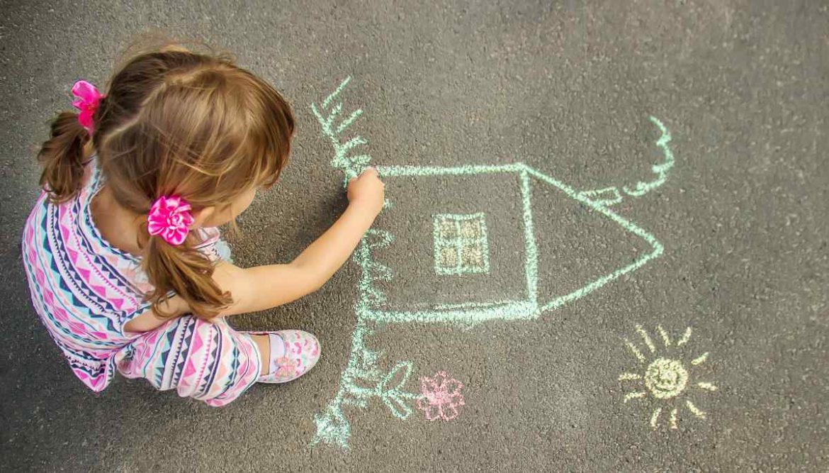 Una niña dibuja en el suelo una casa con una tiza