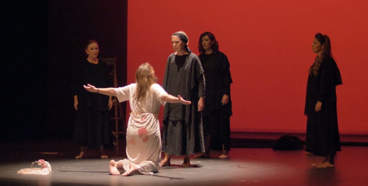 Una representación de una obbra teatral con una mujer de rodillas y otras frente a ella