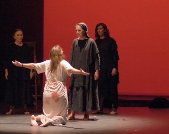 Una representación de una obbra teatral con una mujer de rodillas y otras frente a ella